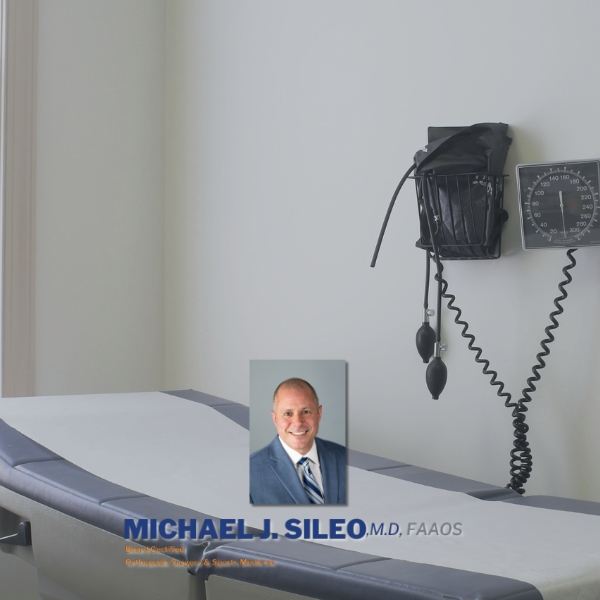 An empty medical exam room with a blood pressure monitor on the wall and a professional headshot of a smiling man labeled “Michael J. Sileo, M.D., FAAOS” overlaid on the image.