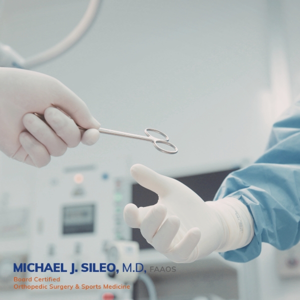 shoulder arthroscopy surgeon in hauppauge dr michael sileo A medical professional hands a surgical instrument to another gloved person in an operating room Text at the bottom highlights the credentials and specialty of a leading Shoulder Arthroscopy Surgeon in Hauppauge